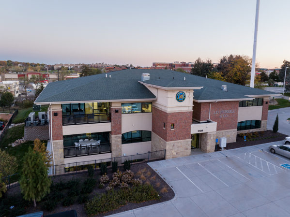 Aerial of brick and stucco office building, that is JDH Omaha headquarters, with buildings and a sunrise sky behind.