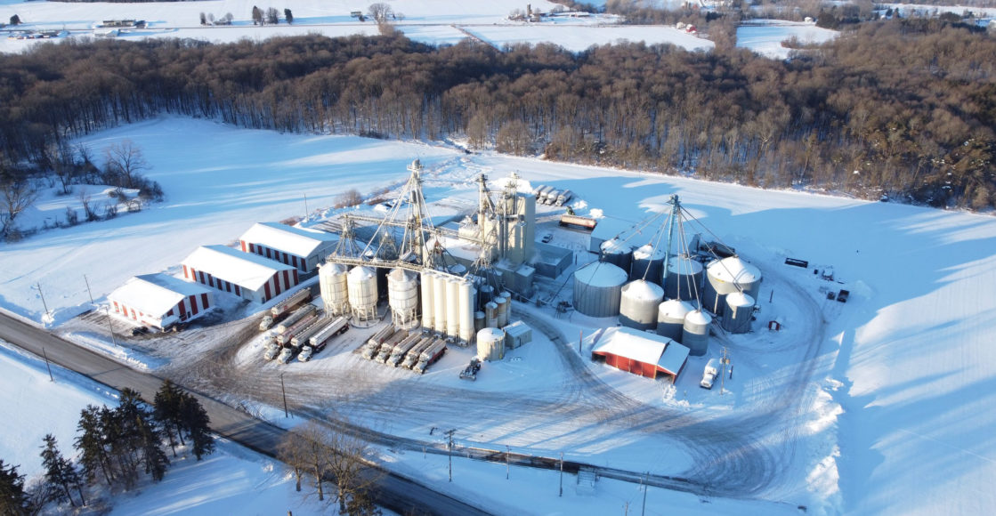 Aerial of Gold Star mill in the winter. There's snow covering the land and you can see car and tractor tracks around the facility.
