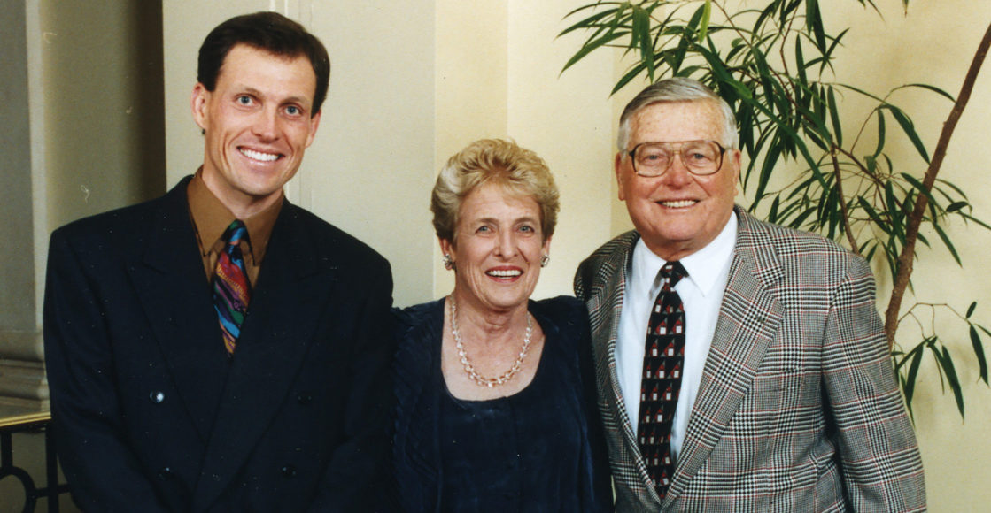Family photo of Scot, Pat and Dale Hillman. They're dressed up and standing close together inside.